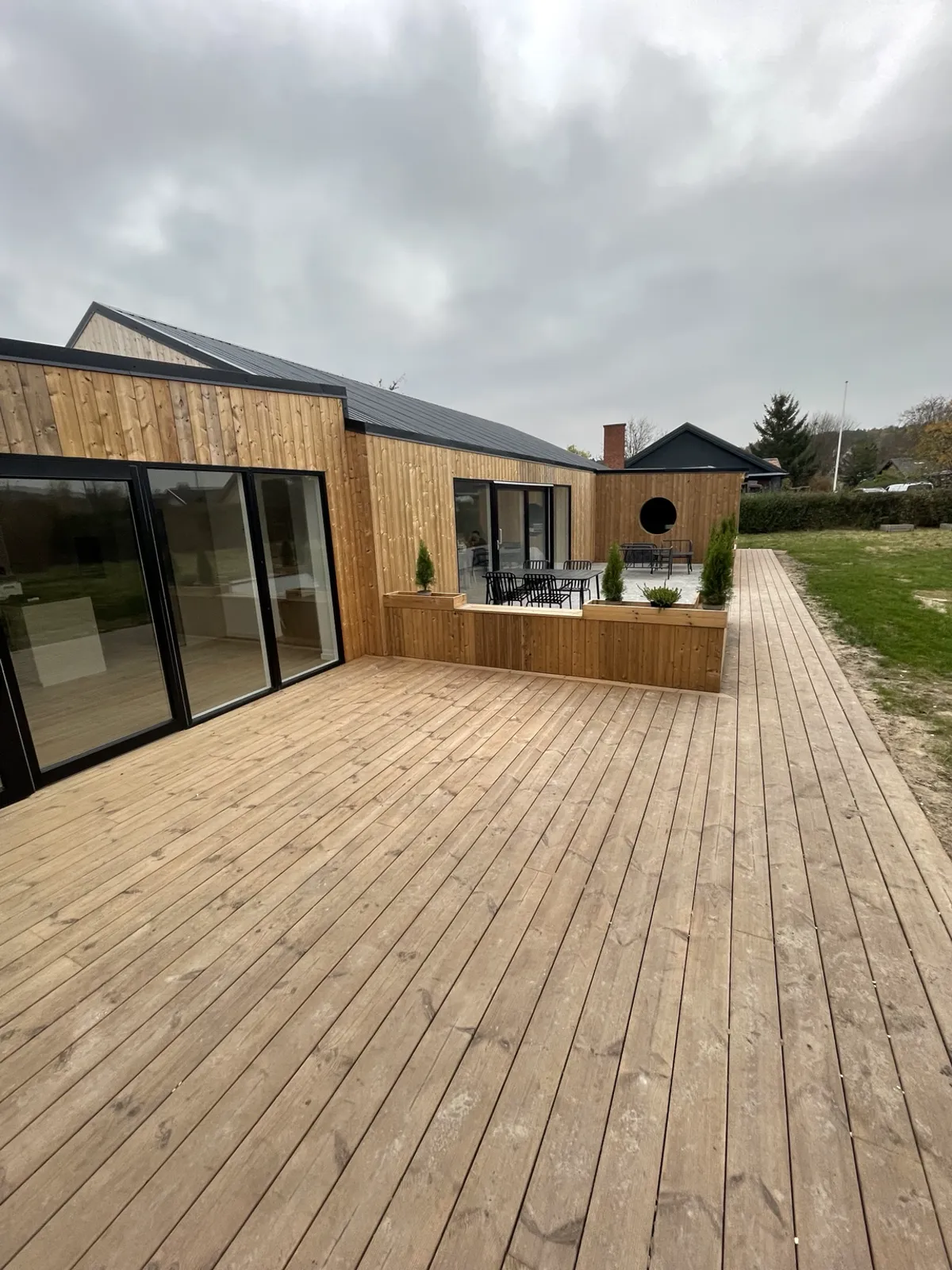 Træbeklædt bolig med store vinduer og en åben træterrasse